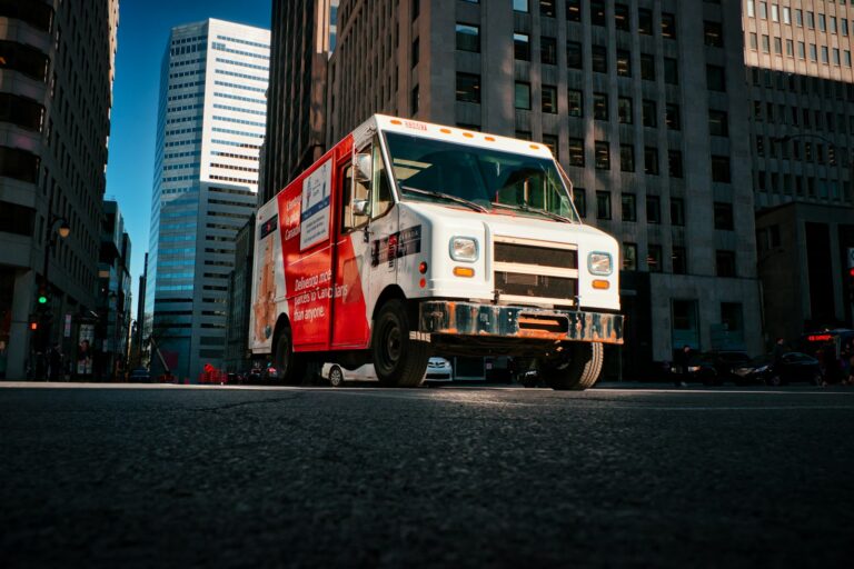 a red and white truck driving down a street next to tall buildings